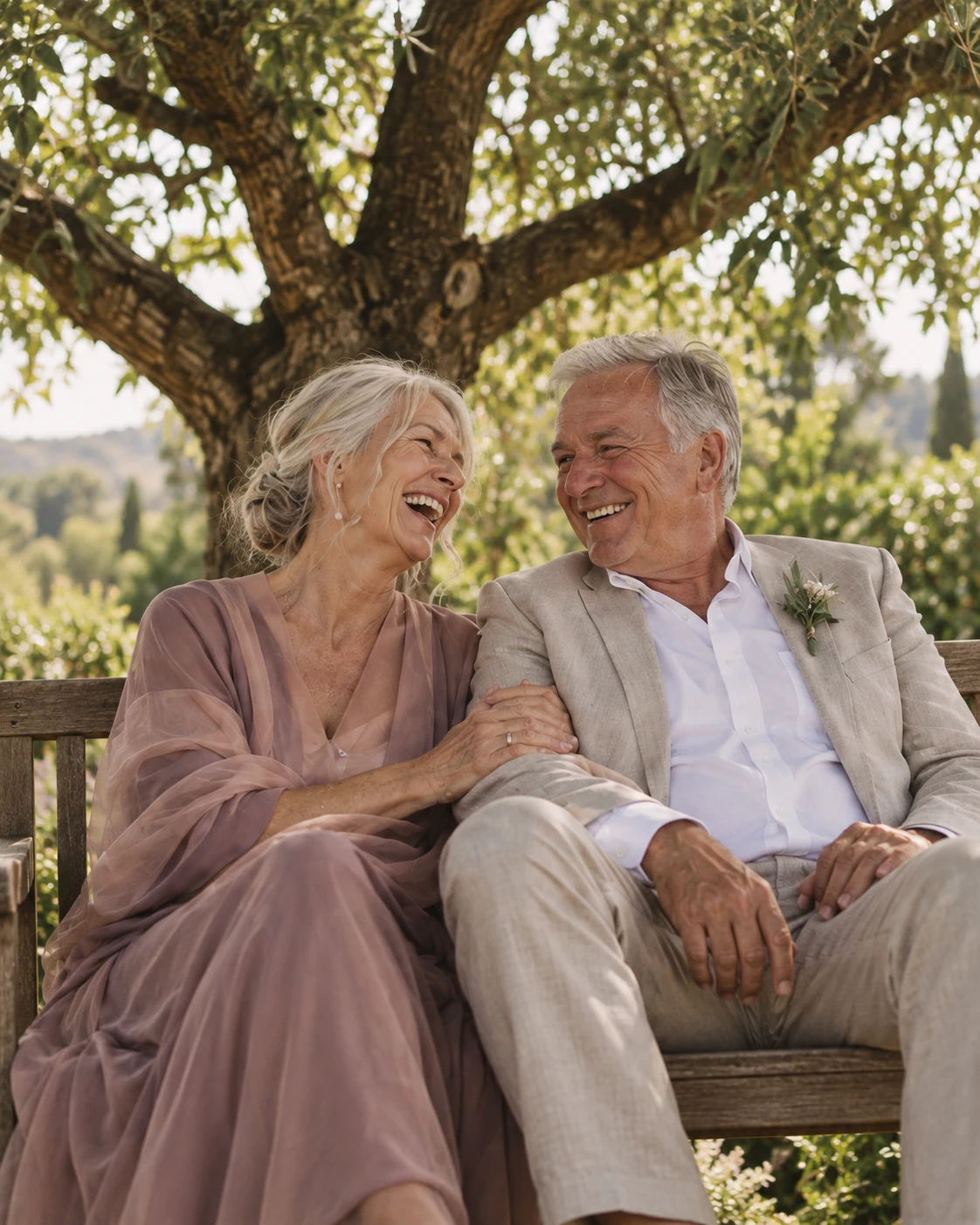 An older husband and wife laughing beneath an olive tree